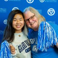 Two alumni pose for a photo with a pom-pom